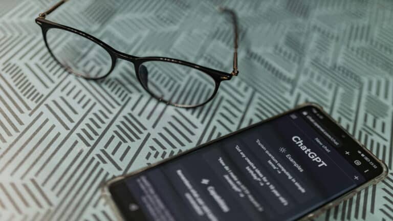 Glasses placed next to a smartphone displaying ChatGPT on a patterned surface.