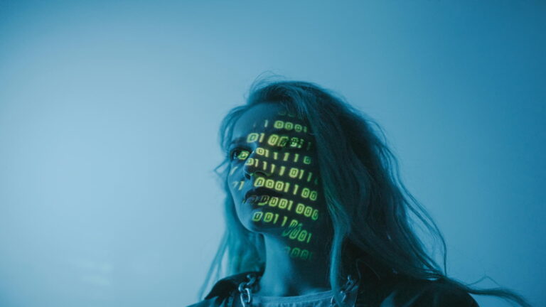 Woman's face illuminated with binary code projections in a blue-lit environment