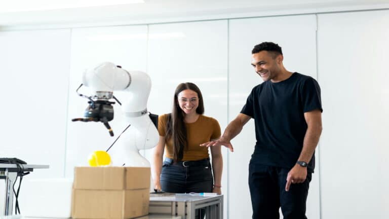 Two individuals interacting with a robotic arm in a modern workspace.