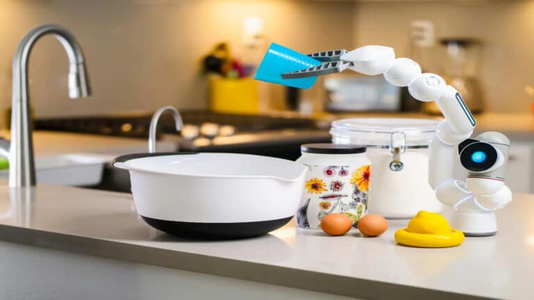 A robotic arm in a modern kitchen holding a blue measuring cup near a bowl and other ingredients.