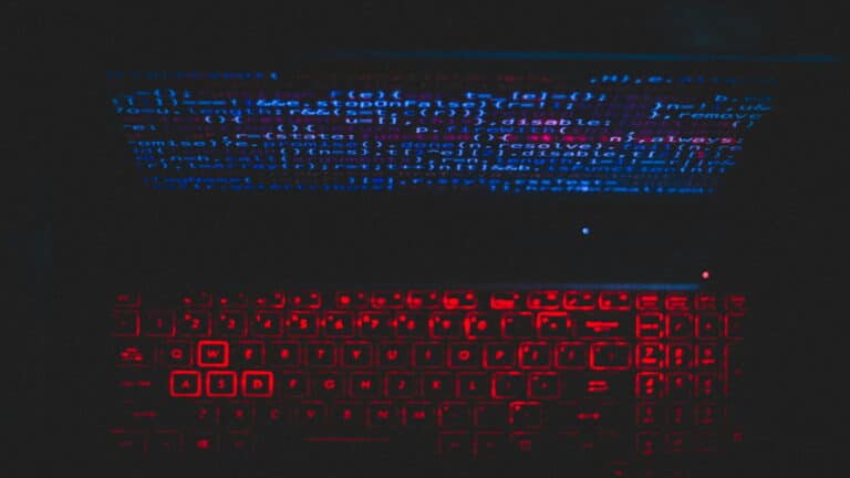 A laptop keyboard with red backlighting and code on the screen