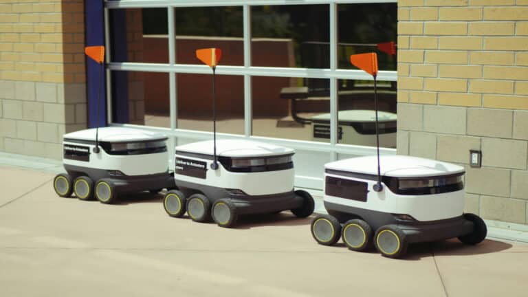 Three delivery robots with antennas parked outside a building