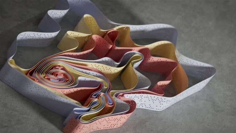 Colorful abstract ribbon-like structure with perforations on a concrete surface.