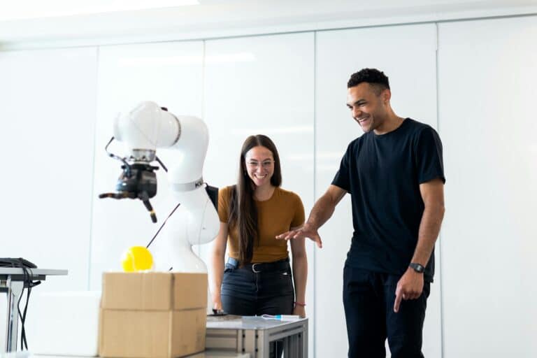 Two professionals collaborating with a robotic arm demonstrating AI for supply chain management